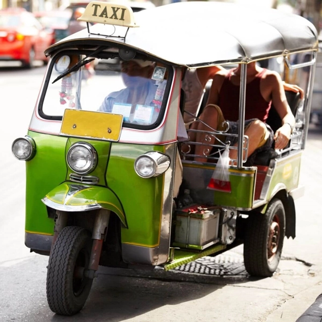Un taxi tuk-tuk circula por la calle, ofreciendo un medio de transporte único y colorido en un animado entorno urbano.