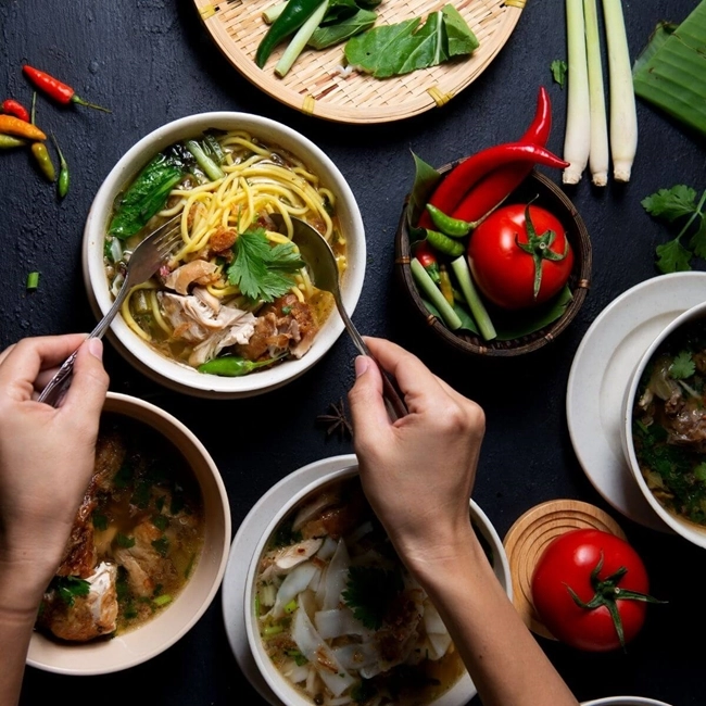Manos que sostienen cuencos de comida con verduras y carne, ilustrando una comida sabrosa y equilibrada.
