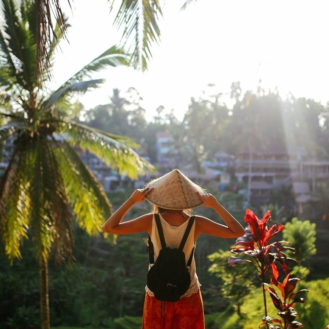 Una mujer con sombrero y pantalones cortos está de pie en una colina, admirando un pintoresco pueblo.